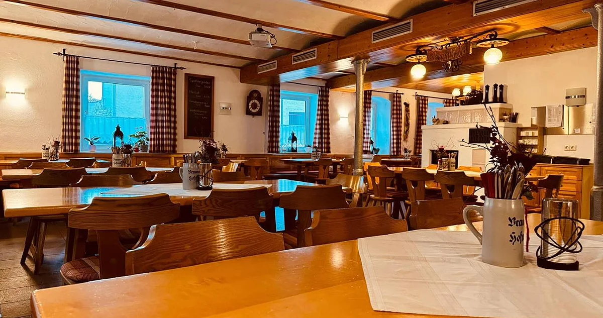 Gastraum mit Holztischen und -stühlen, karierten Vorhängen an Fenstern und dekorativen Krügen auf den Tischen